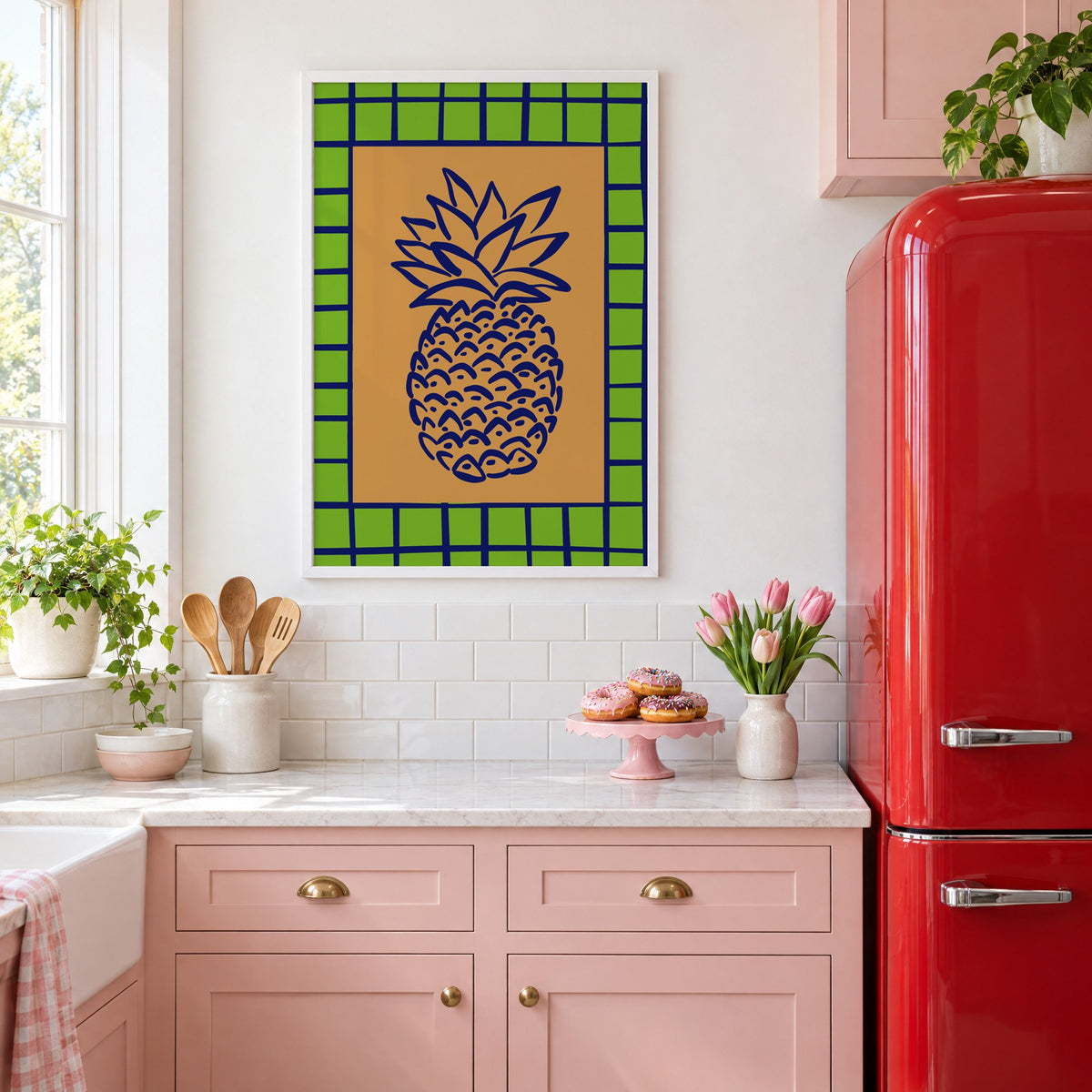 Pineapple navy line on ochre with green grid print in a white frame above pink cabinets beside a red retro fridge