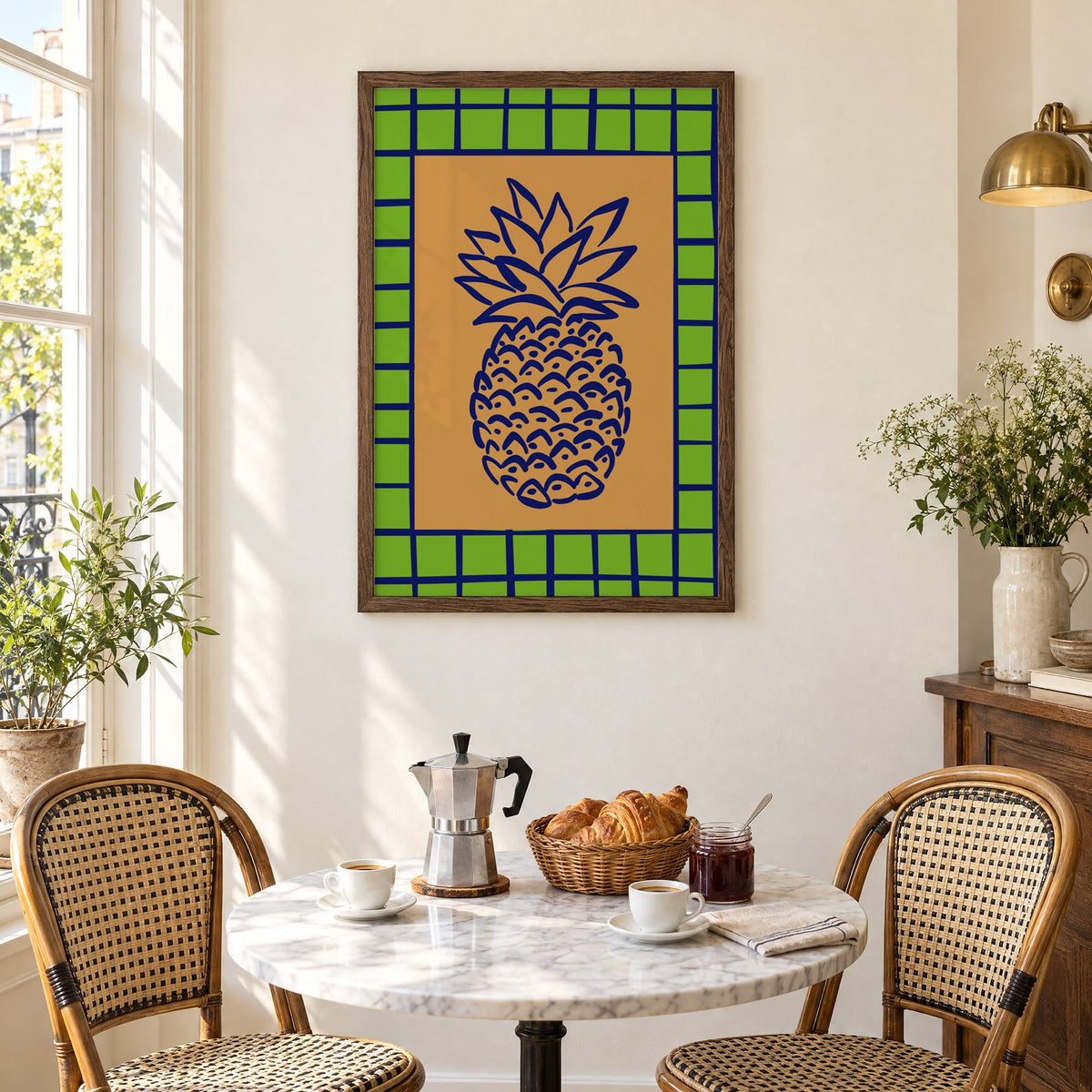 Pineapple navy line on ochre with green grid print in a walnut frame above a marble bistro table with croissants and rattan chairs