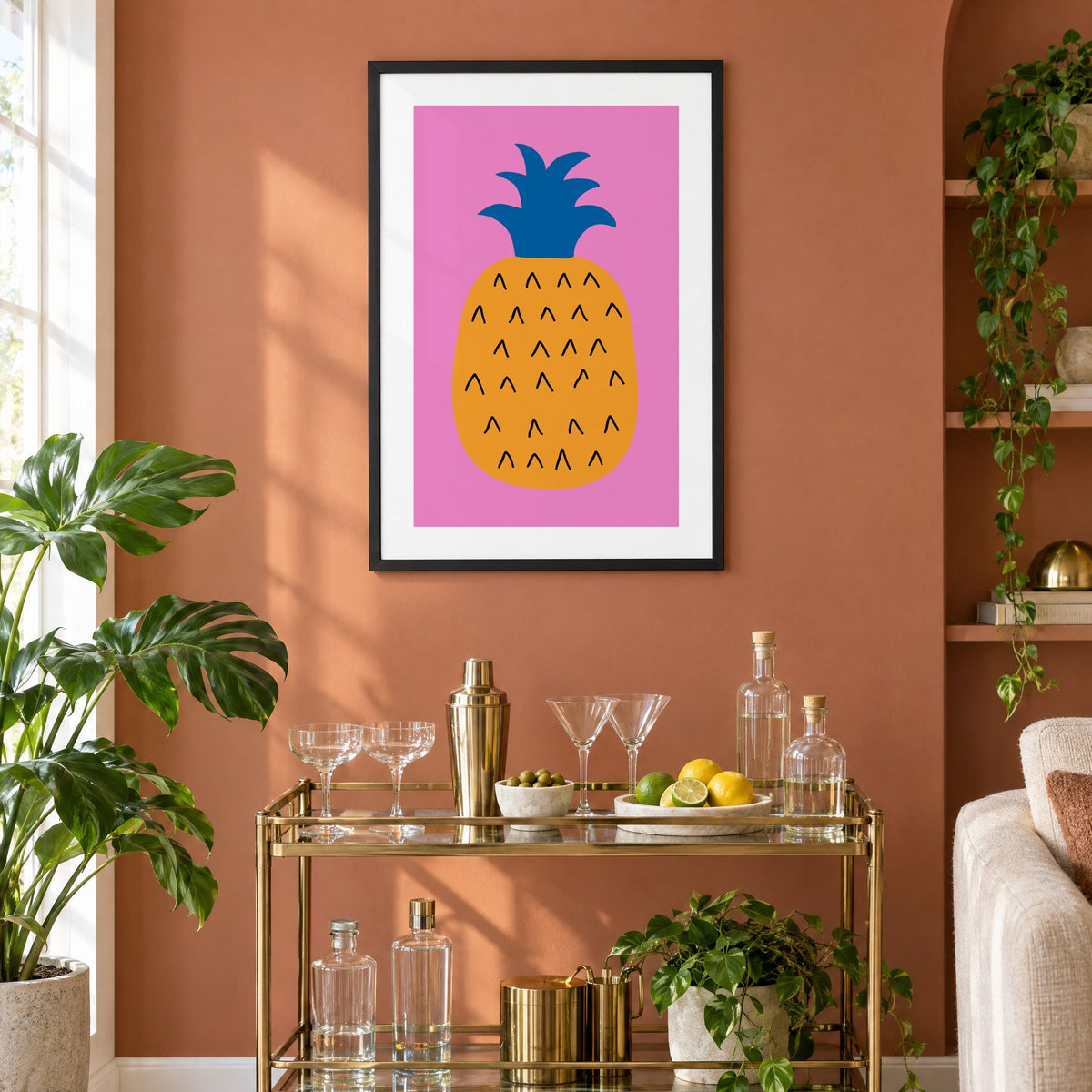 orange pineapple cobalt crown hot pink print in a black frame on a terracotta wall above a brass bar cart with coupes and citrus