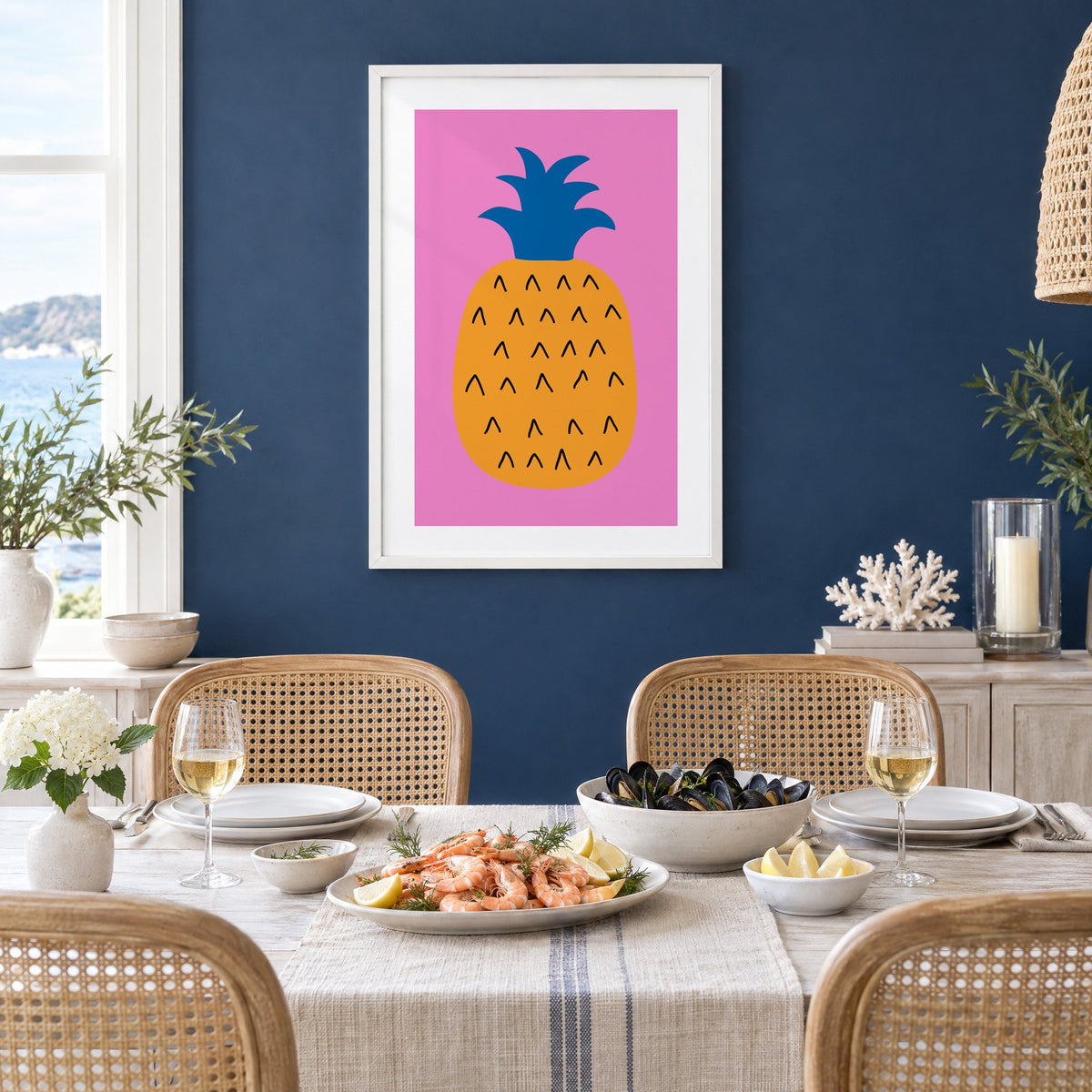 orange pineapple cobalt crown hot pink print in a white frame on a navy wall above a dining table set with shrimp and mussels