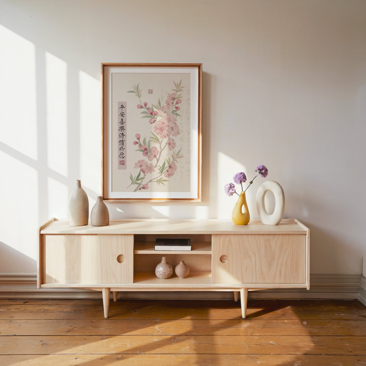pink blossom with calligraphy blessing print shown in a wood frame with a white mat above a pale wood media console