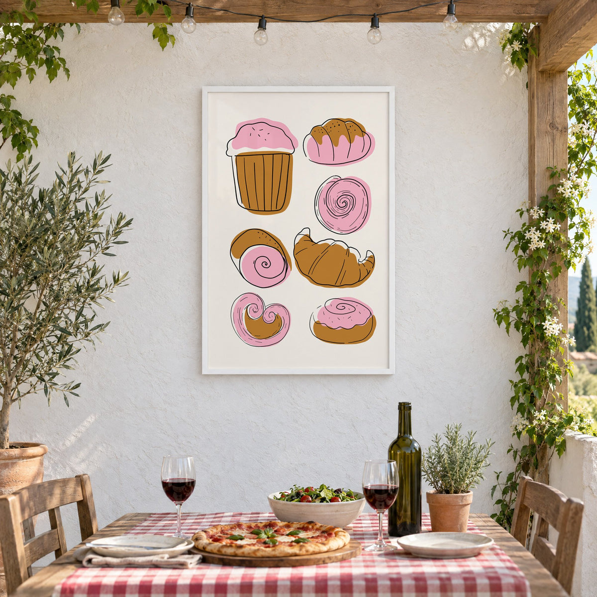 Pink and brown pastries doodle print in a white frame on a stucco wall above a checked-cloth table with pizza and red wine