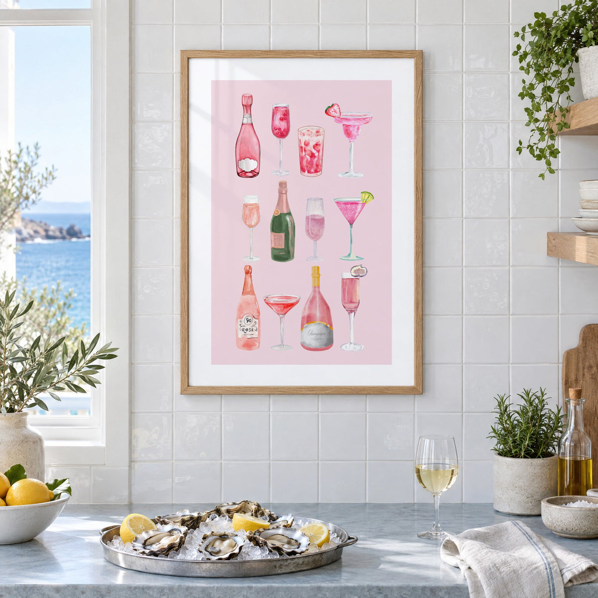 pink champagne bottles and cocktails watercolor print in an oak frame on white tiles above a marble counter with oysters and lemons by a sea view