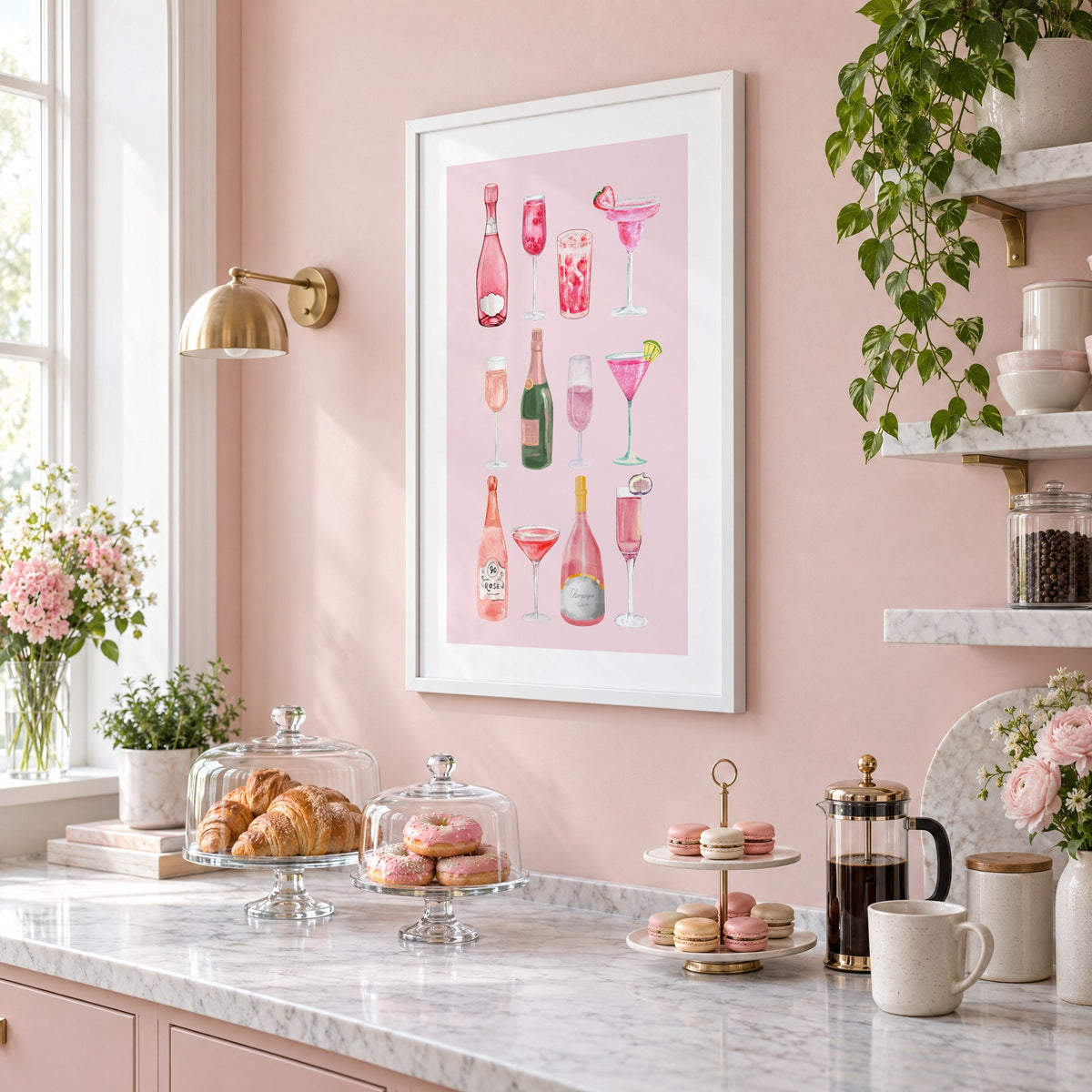 pink champagne bottles and cocktails watercolor print in a white frame on a blush pink wall above a patisserie counter with croissants and macarons, seen at an angle
