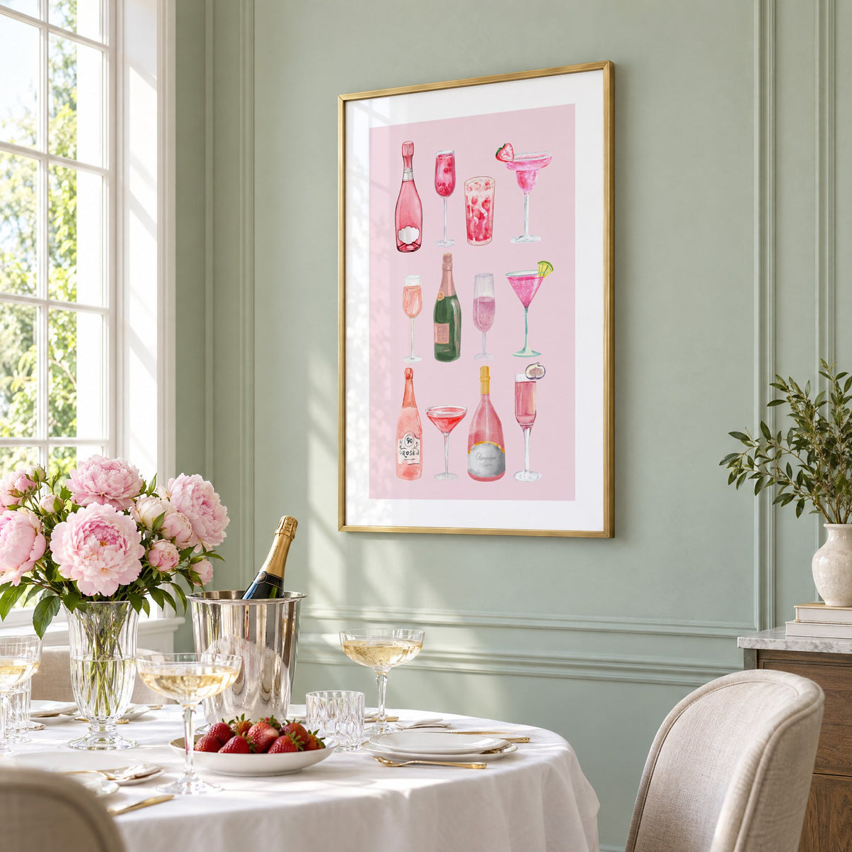 pink champagne bottles and cocktails watercolor print in a brass frame on a sage wall above a brunch table with champagne and peonies, seen at an angle