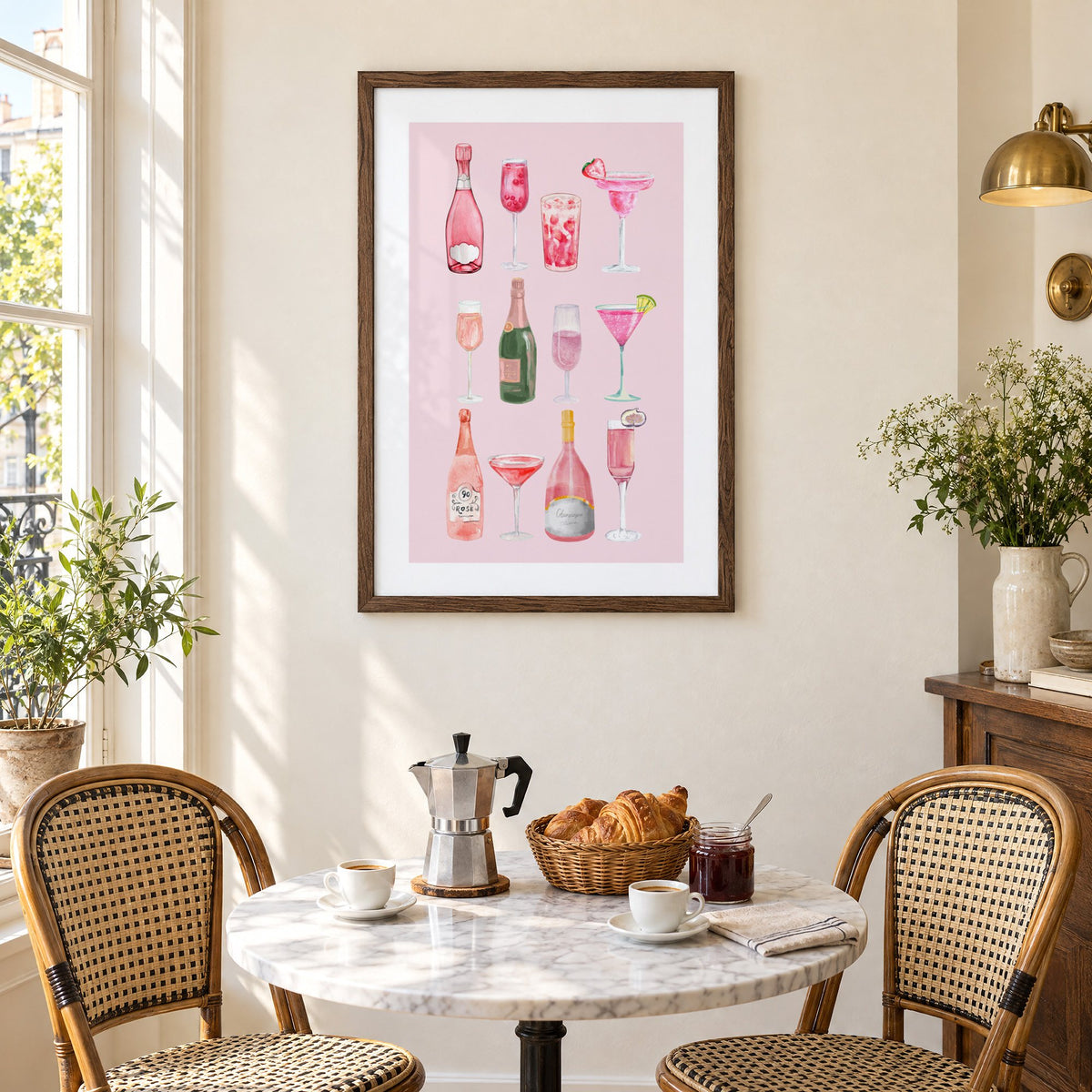 pink champagne bottles and cocktails watercolor print in a walnut frame above a marble bistro table with croissants and rattan chairs