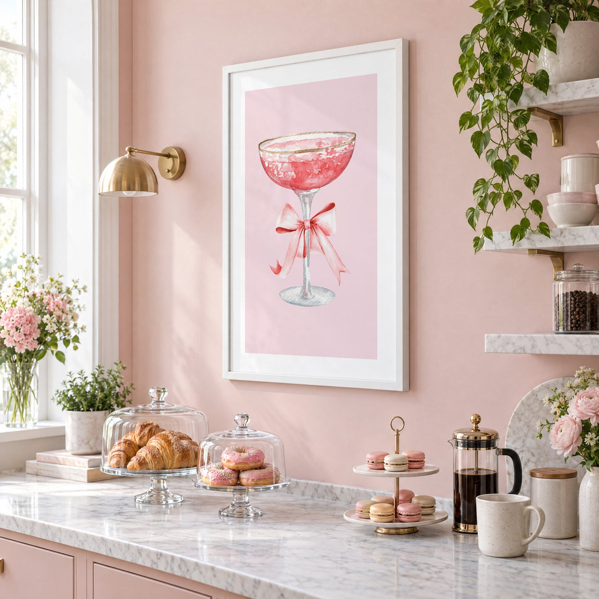 gold rim champagne coupe satin bow print in a white frame on a blush pink wall above a patisserie counter with croissants and macarons, seen at an angle