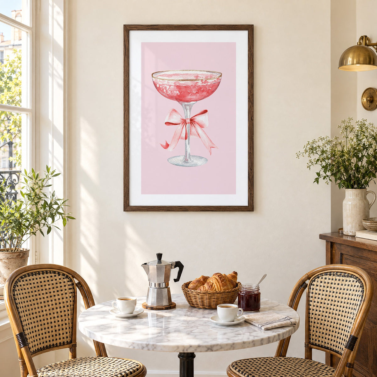 gold rim champagne coupe satin bow print in a walnut frame above a marble bistro table with croissants and rattan chairs