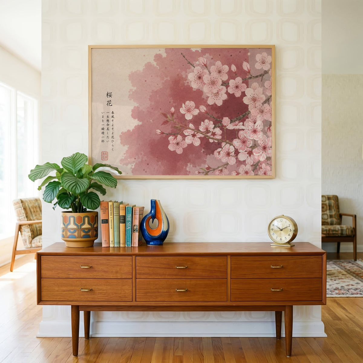 Pink cherry blossom with Japanese verse print in a light oak frame above a teak credenza with books and a brass clock