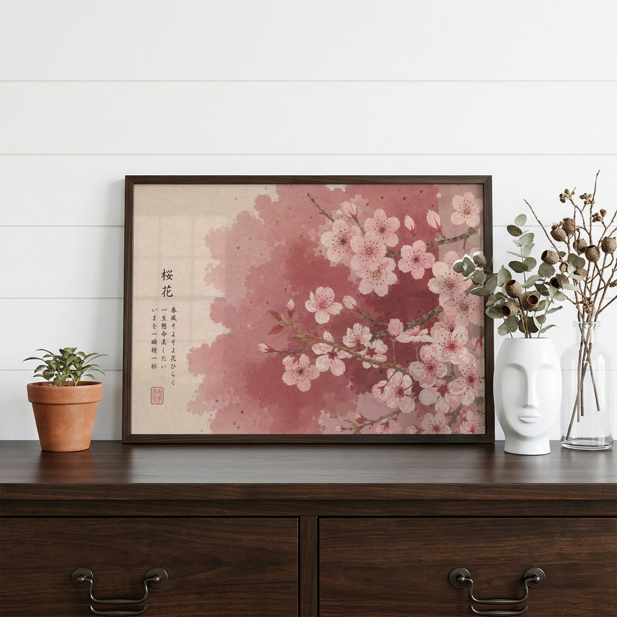 Pink cherry blossom with Japanese verse print in a dark walnut frame on a dark wood dresser beside a white face vase