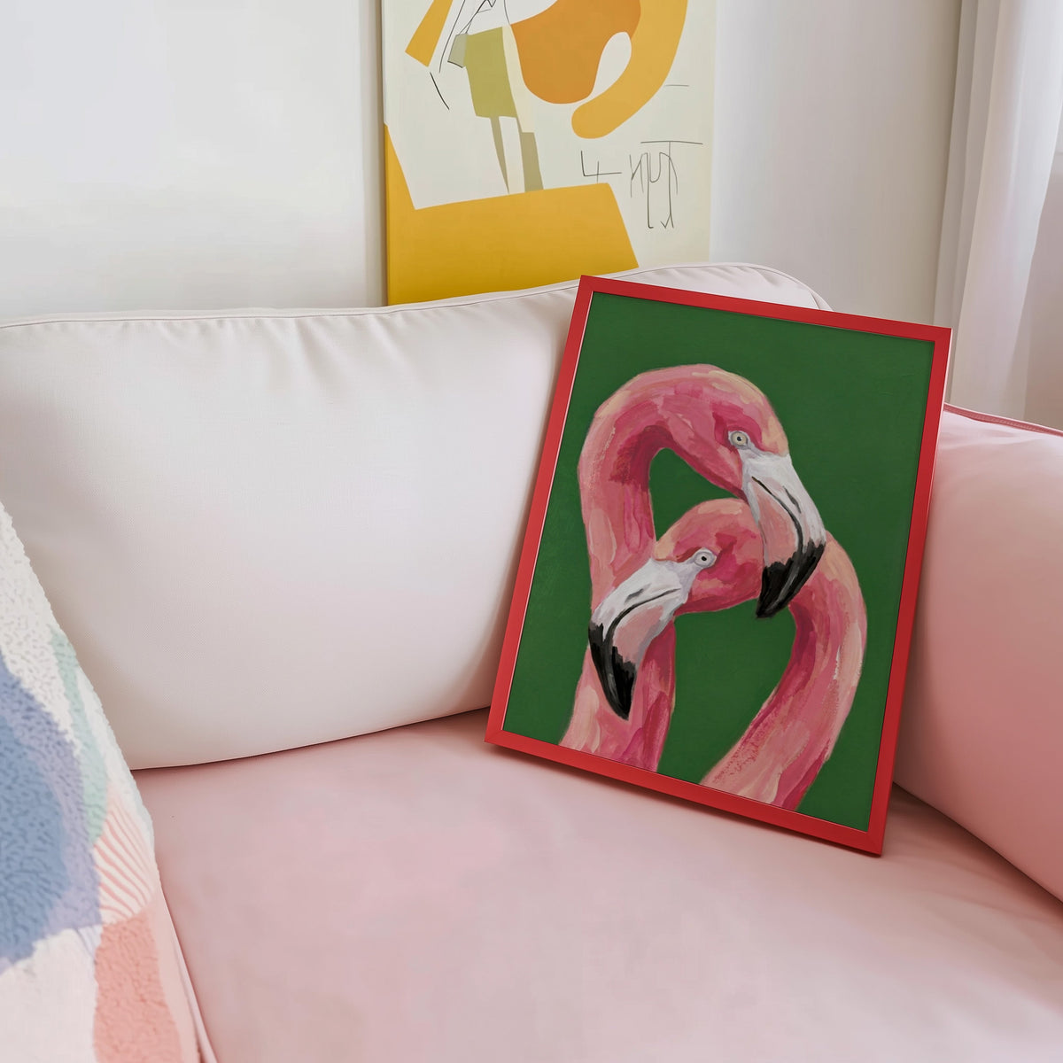 Entwined flamingos print shown in a red frame leaning on a blush pink sofa