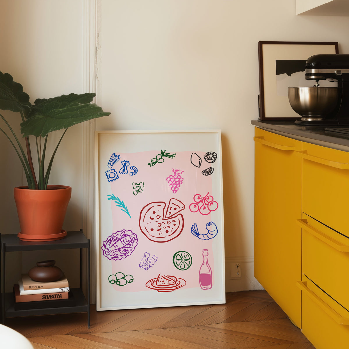 Food doodle print in a white frame leaning on parquet beside a bright yellow kitchen