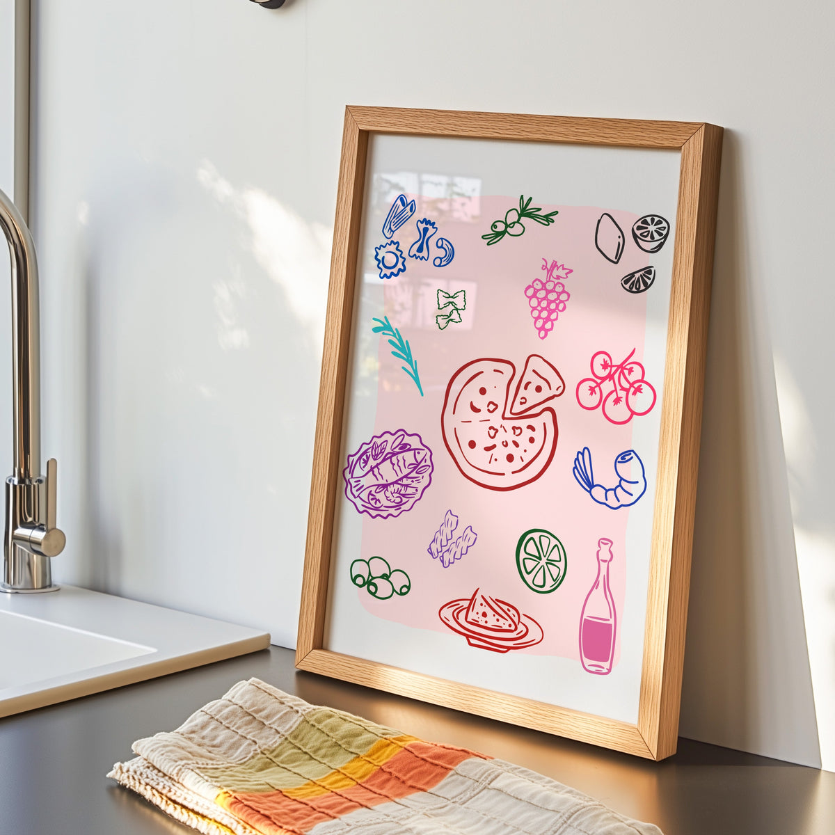 Food doodle print in an oak frame by the kitchen sink beside a striped tea towel