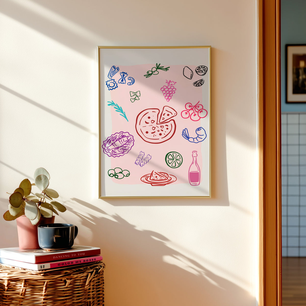 Food doodle print in a gold frame above a basket of books and a pilea plant