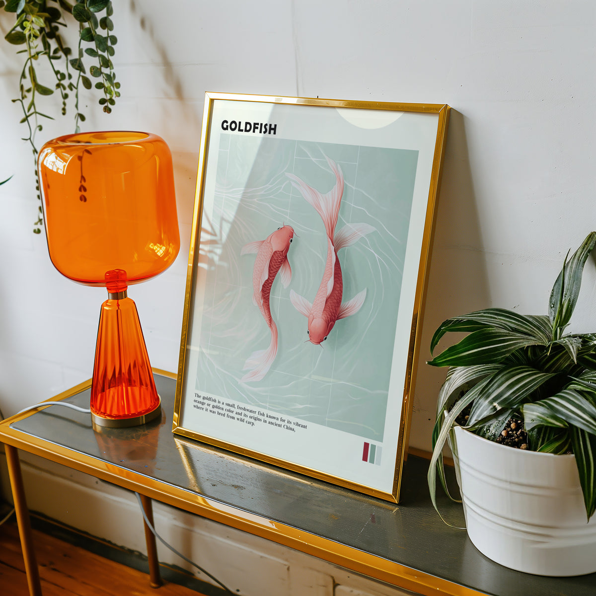 Pink goldfish pair on mint water print shown in a gold frame on a console beside an orange glass lamp