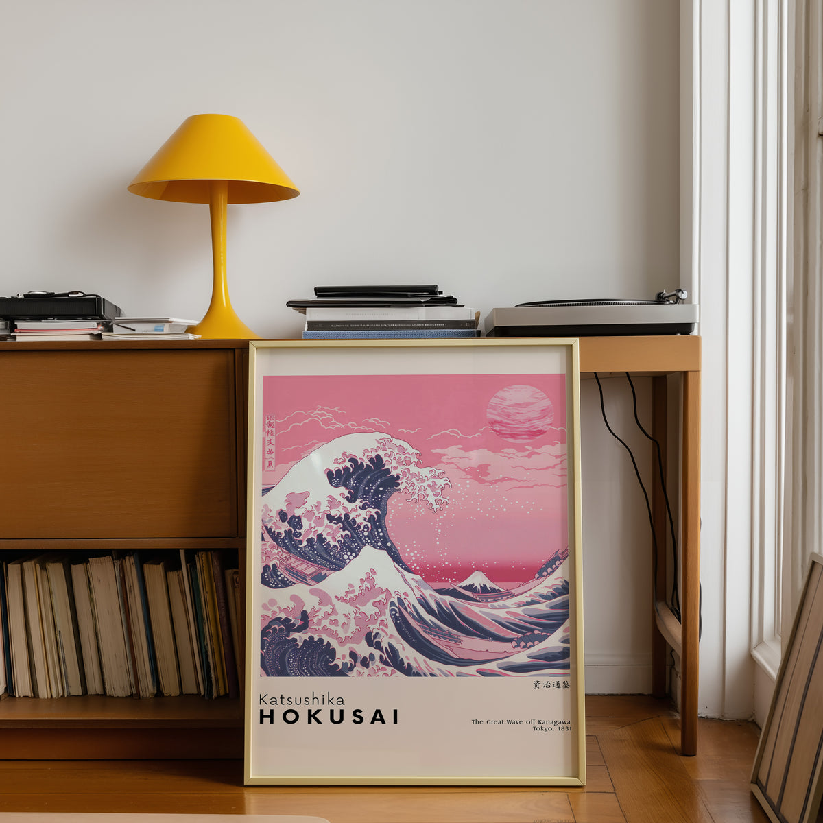 Pink Great Wave off Kanagawa print shown in a gold frame below a teak desk with a yellow lamp