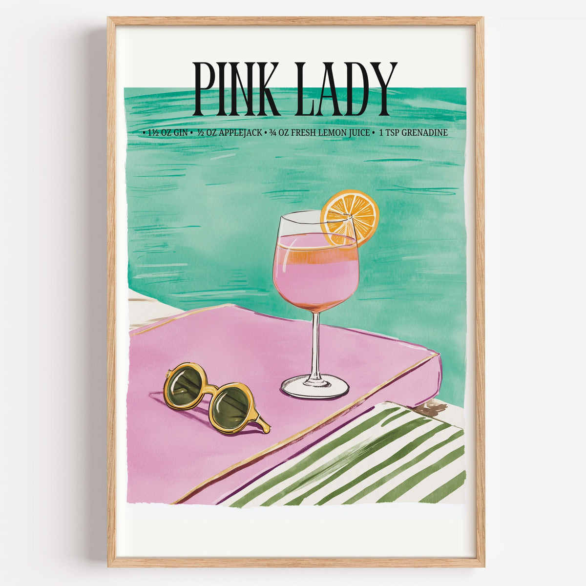 Pink Lady cocktail recipe print in a light oak frame on a plain white wall