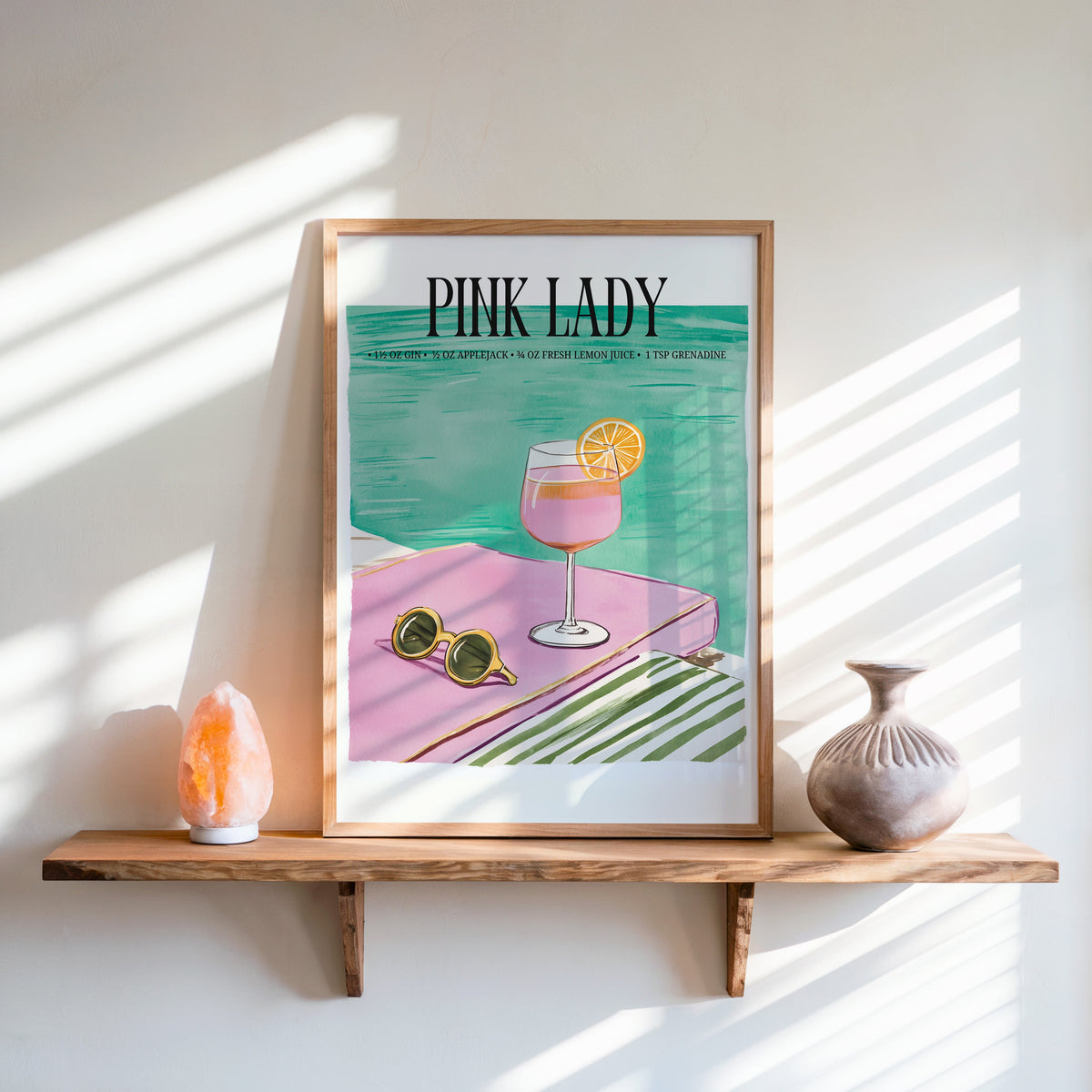 Pink Lady cocktail print in an oak frame on a live-edge shelf beside a salt lamp