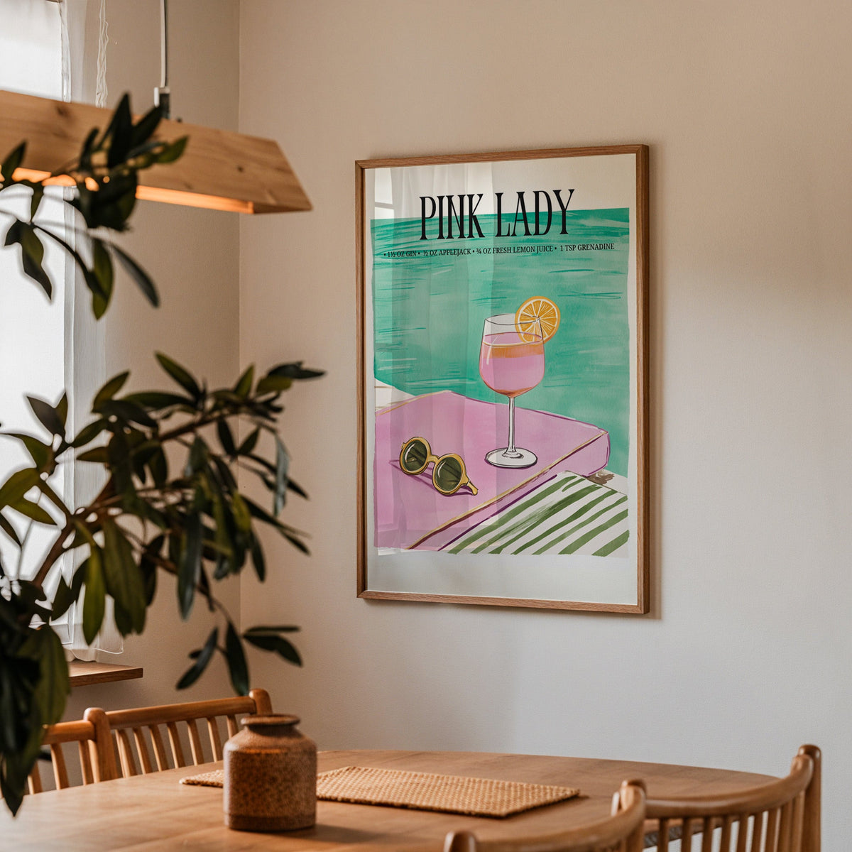 Pink Lady cocktail print in a walnut frame above a dining table with olive branches