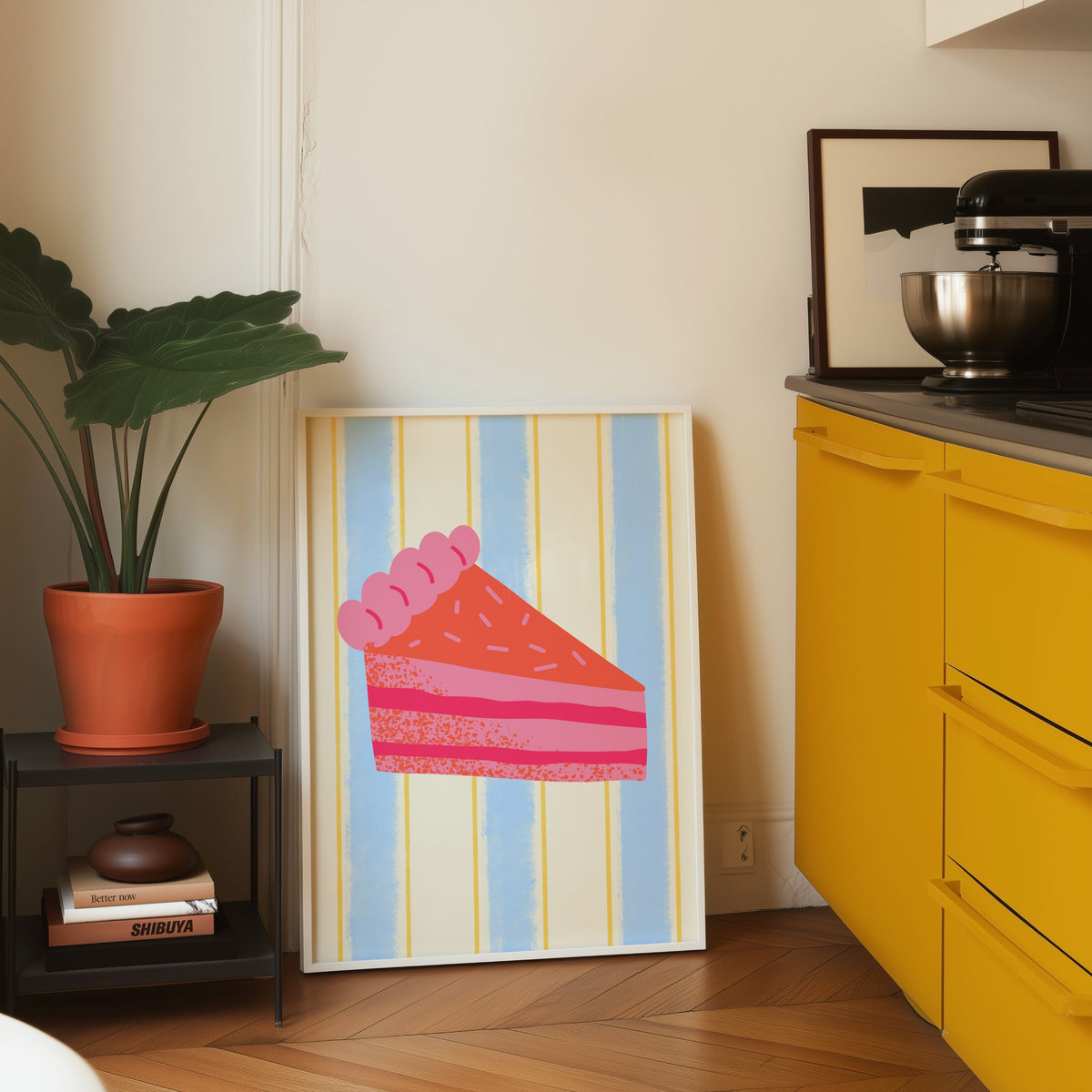 Pink layer cake print in a white frame on parquet beside a bright yellow kitchen