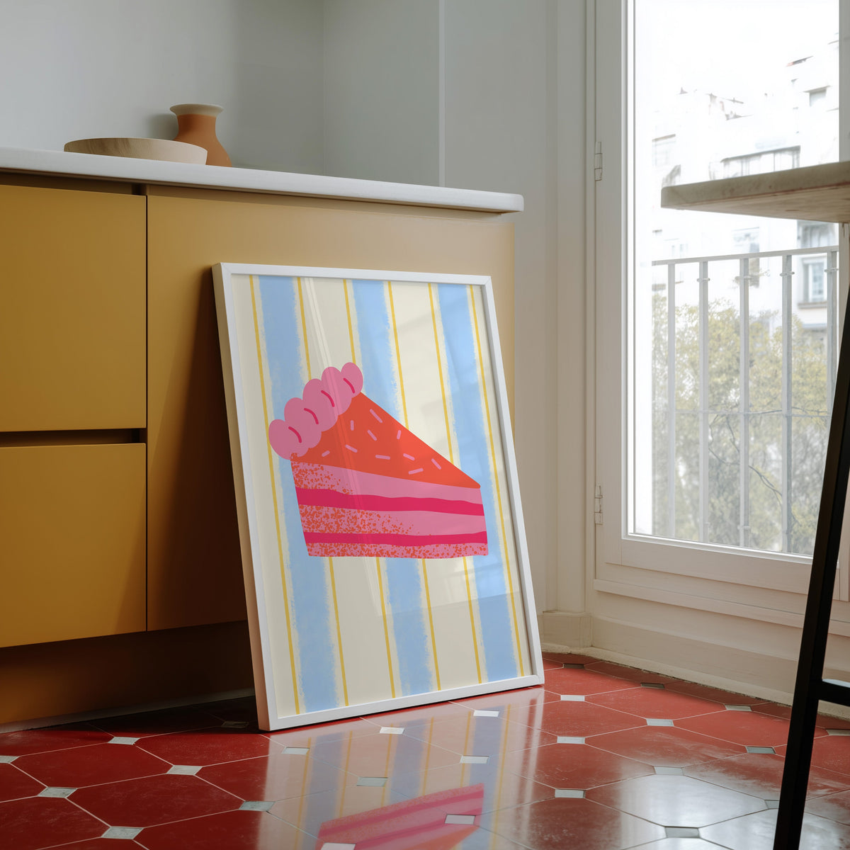 Pink layer cake print in a white frame against yellow cabinets on red tiles