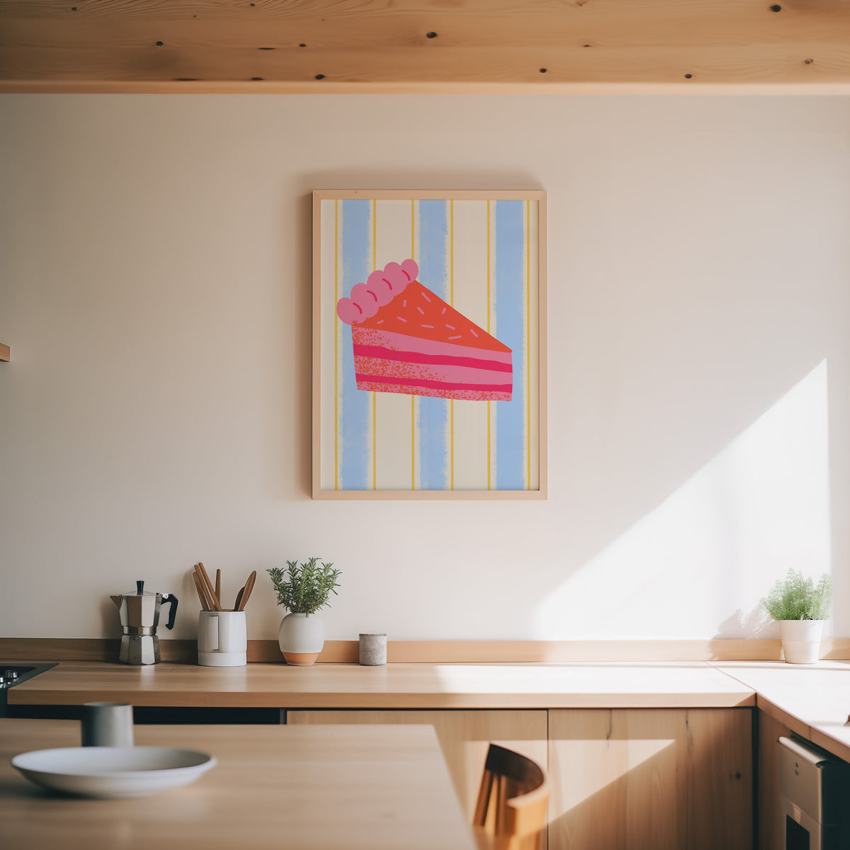 Pink layer cake print in an oak frame above a wood counter with a moka pot