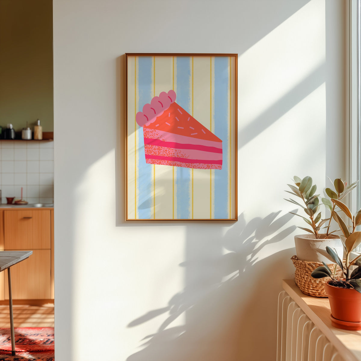 Pink layer cake print in a gold frame in sunlight with plants and a kitchen beyond