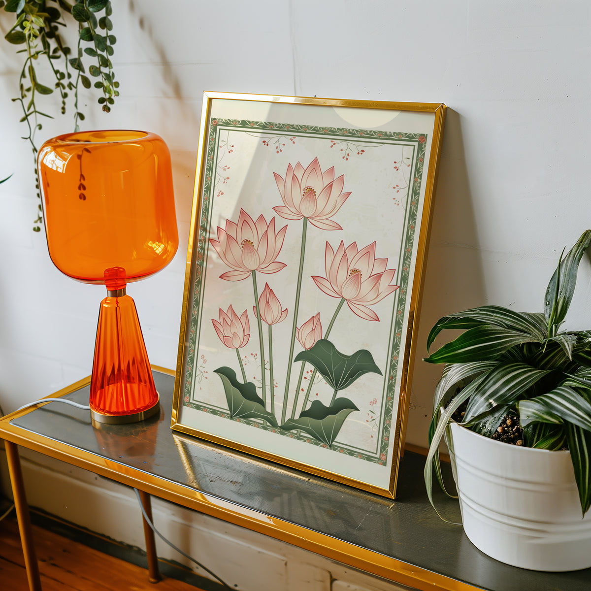 Five pink lotus flowers print shown in a gold frame on a console beside an orange glass lamp