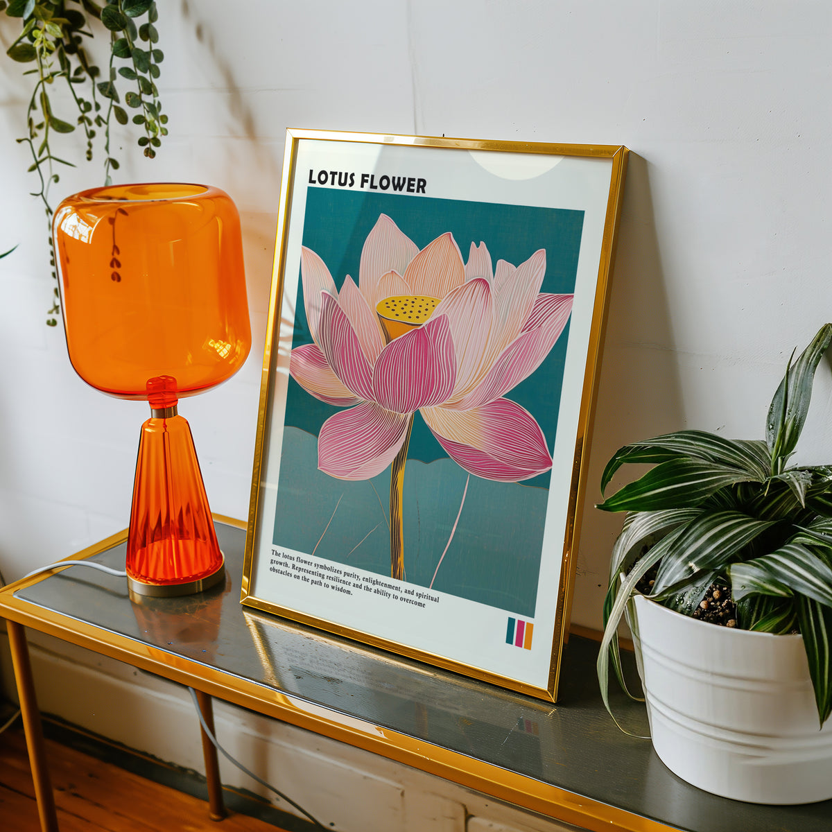Single pink lotus on teal print shown in a gold frame on a console beside an orange glass lamp