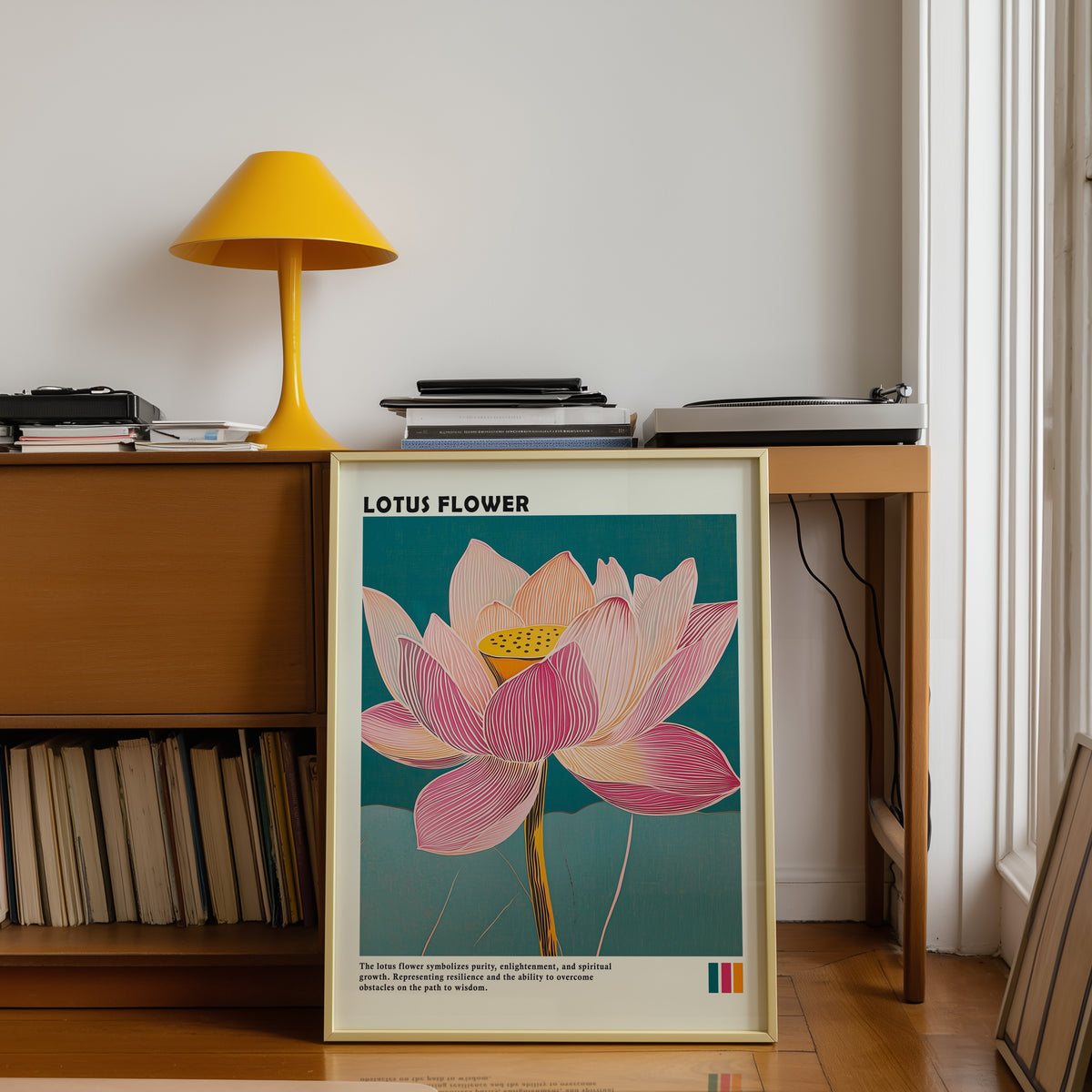 Single pink lotus on teal print shown in a gold frame below a teak desk with a yellow lamp