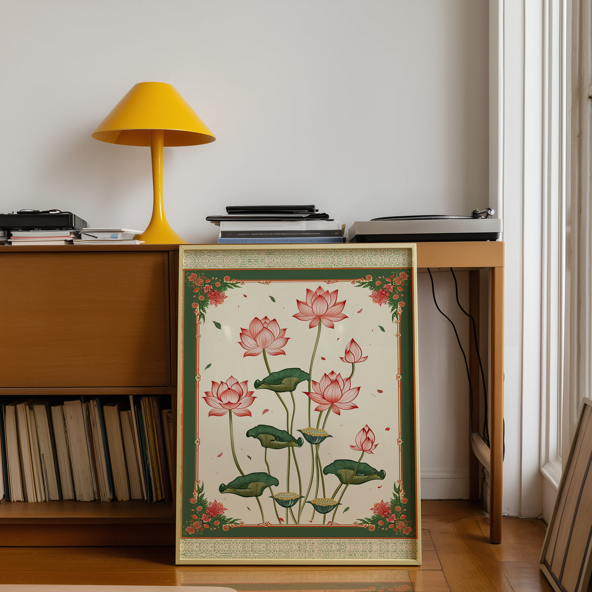 Pink lotus with green ornamental border print shown in a gold frame below a teak desk with a yellow lamp