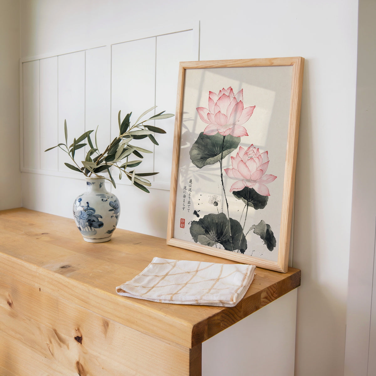 pink lotus ink painting with proverb print in a pine frame on a wooden counter beside a blue and white porcelain vase