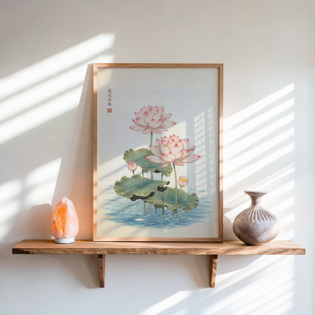 pink lotus pond print in an oak frame on a live-edge wall shelf with a salt lamp and clay vase