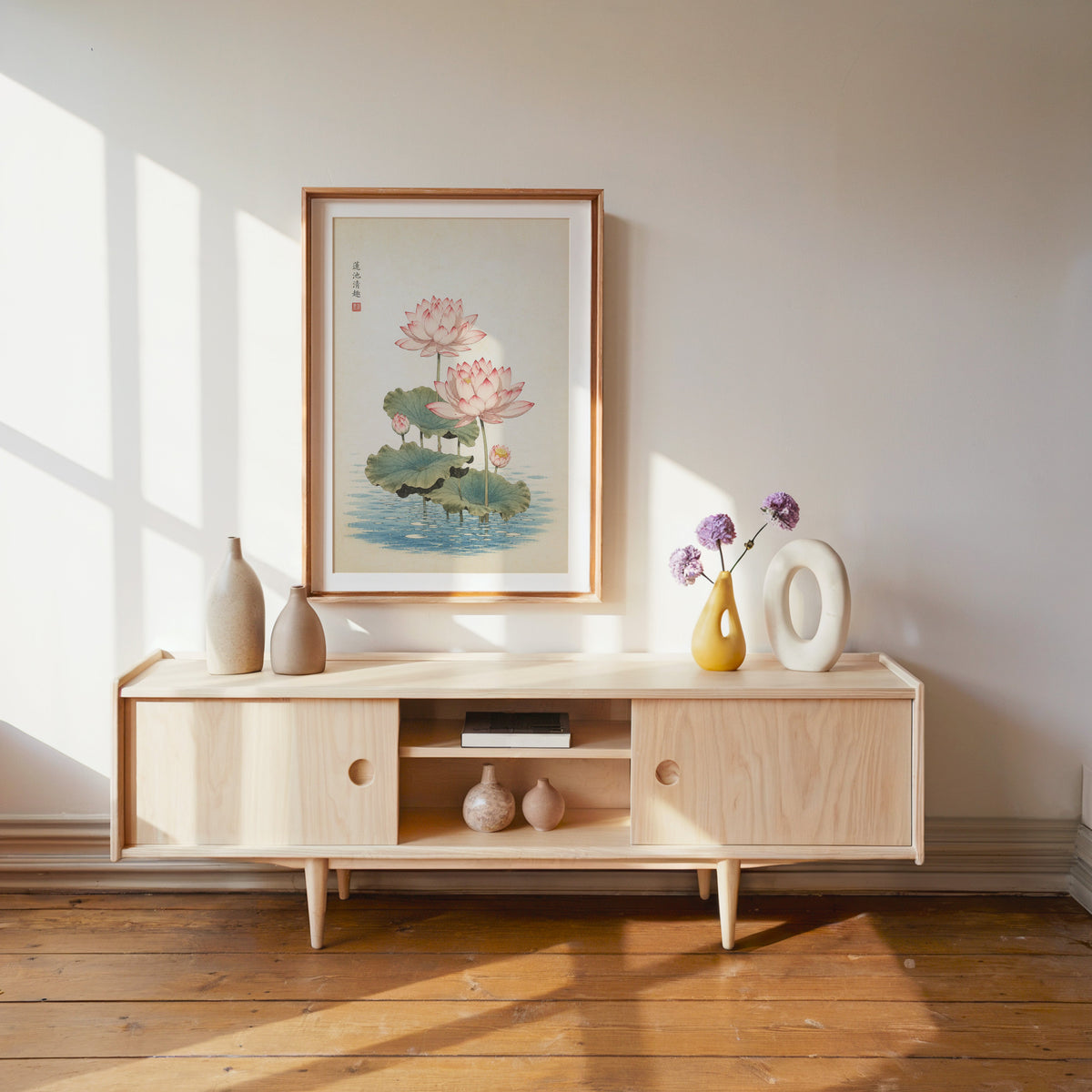 pink lotus pond print shown in a wood frame with a white mat above a pale wood media console