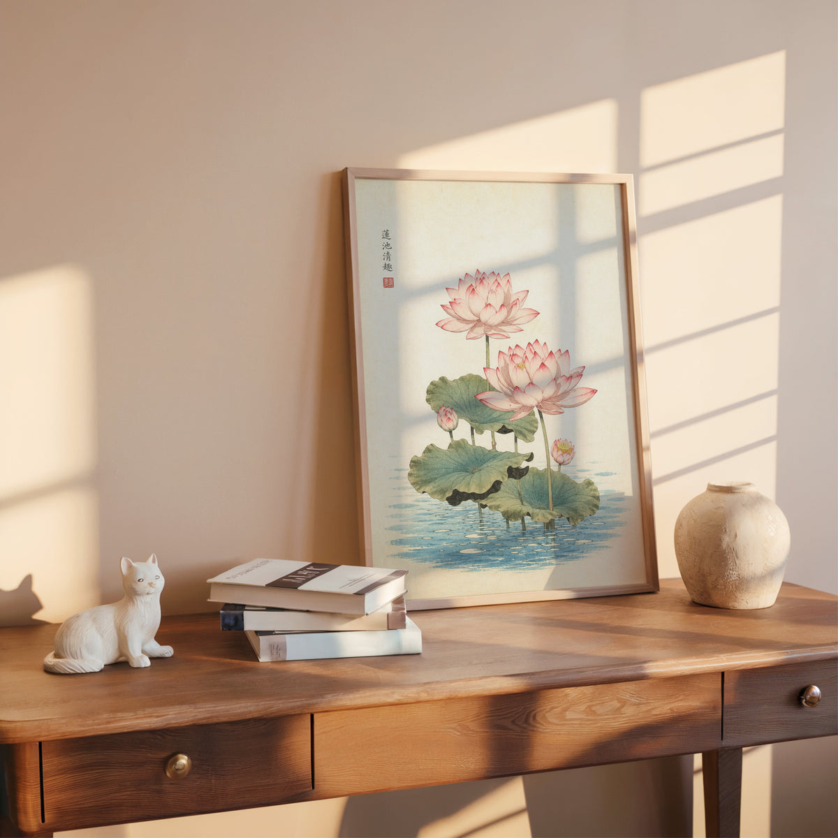 pink lotus pond print shown in a rose gold frame leaning on a wooden writing desk with books