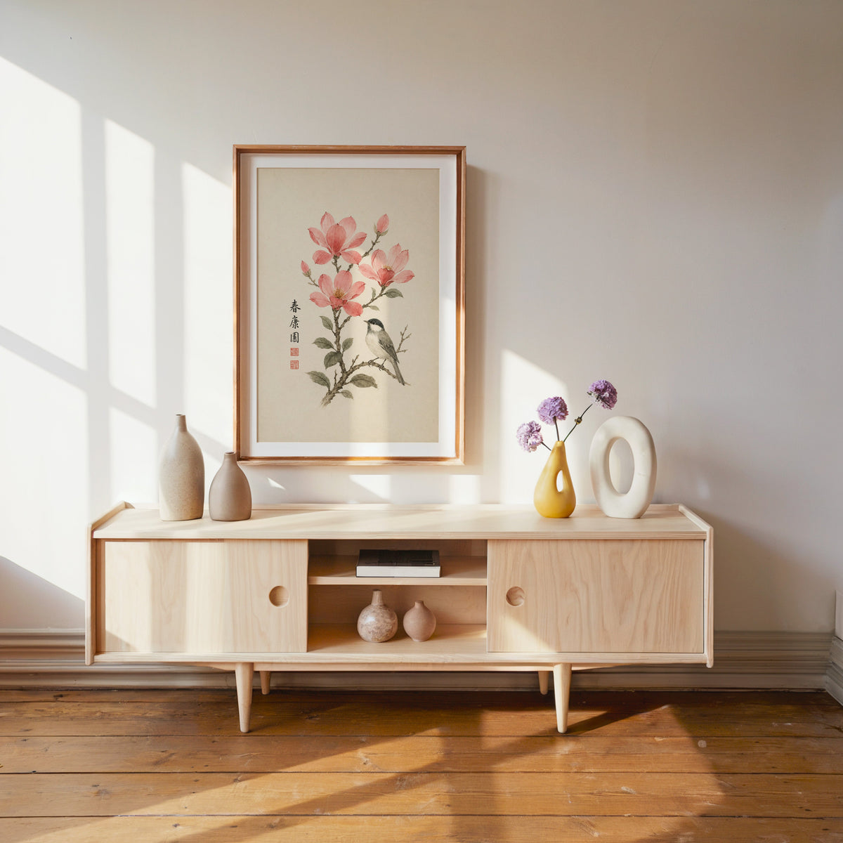 songbird on pink blossom branch print shown in a wood frame with a white mat above a pale wood media console