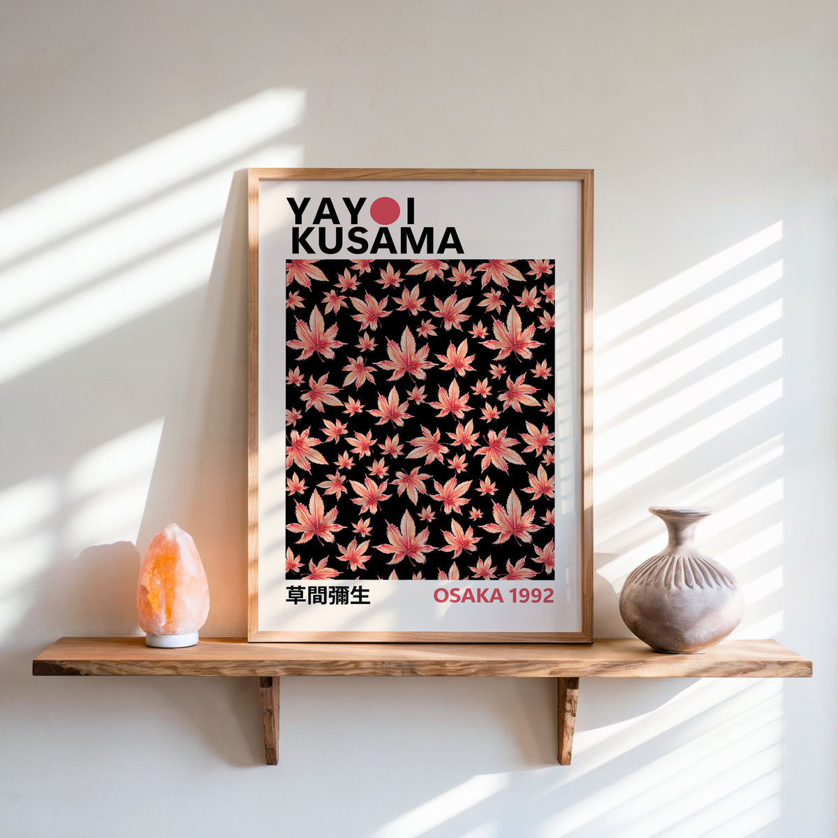 Yayoi Kusama inspired pink maple leaves on black print in an oak frame on a live edge shelf beside a salt lamp