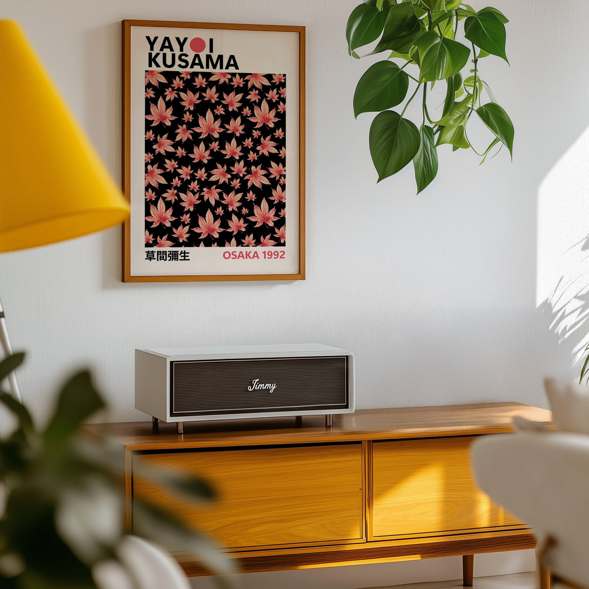Yayoi Kusama inspired pink maple leaves on black print in an oak frame above a teak sideboard with pothos