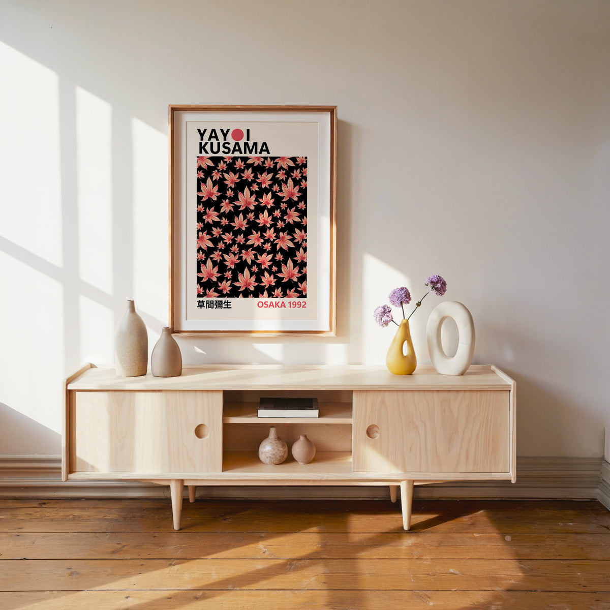 Yayoi Kusama inspired pink maple leaves on black print in a wood frame with white mat over a pale media console