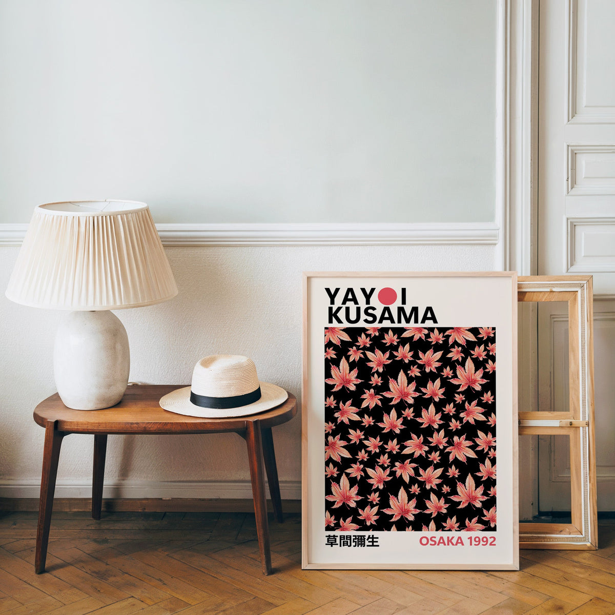 Yayoi Kusama inspired pink maple leaves on black print in an oak frame over a bench with a panama hat