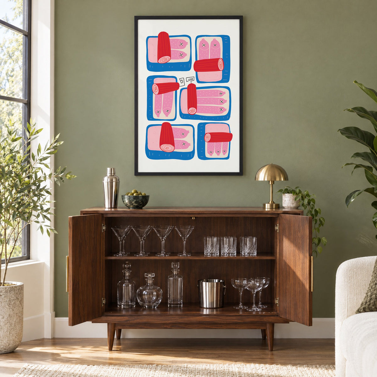 Six blue sardine tins pink fish print in a black frame on an olive green wall above a walnut bar cabinet with glassware