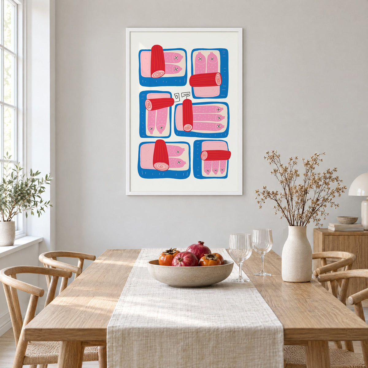 Six blue sardine tins pink fish print in a white frame above a light oak dining table with a linen runner and fruit bowl