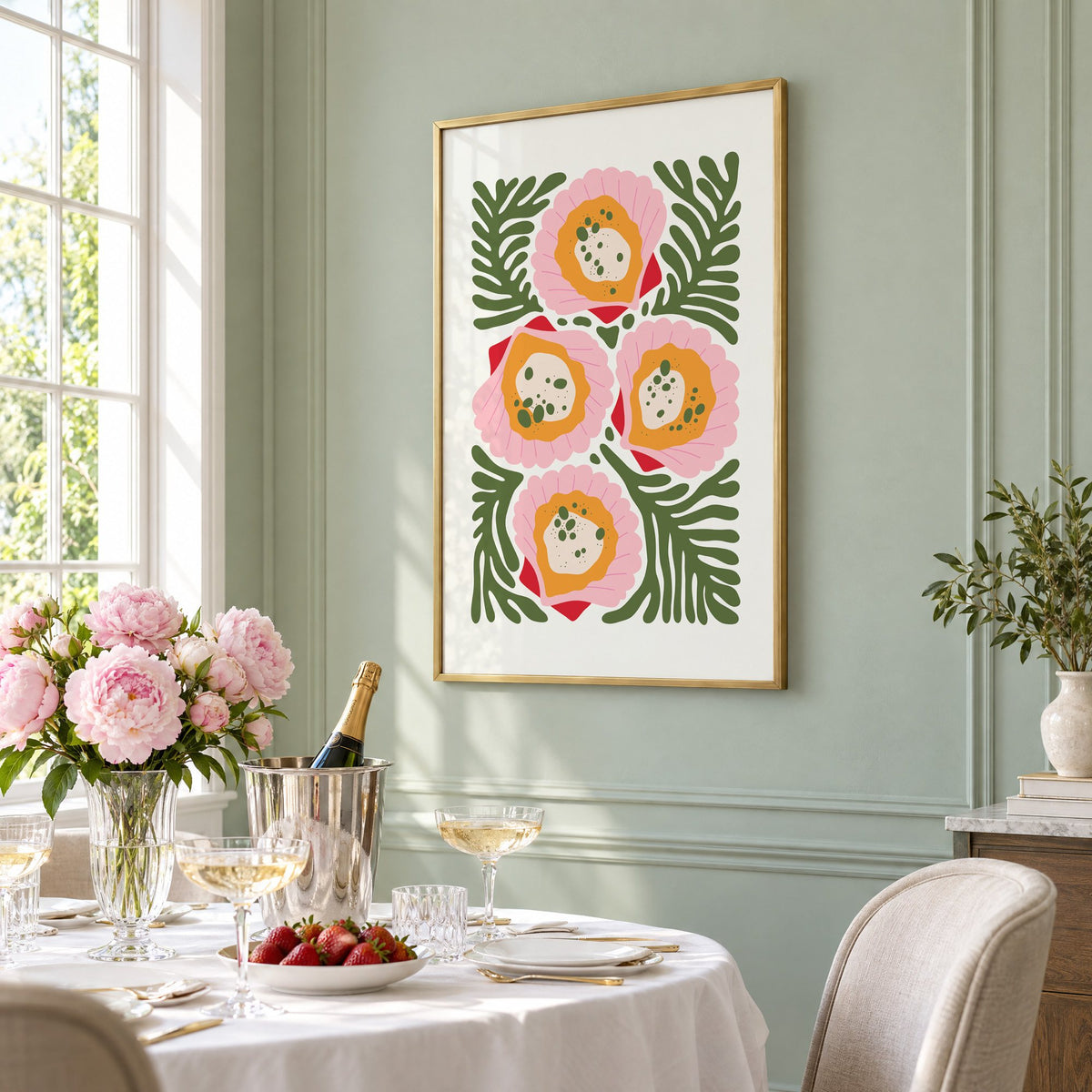pink scallop shells green seaweed print in a brass frame on a sage wall above a brunch table with champagne and peonies, seen at an angle