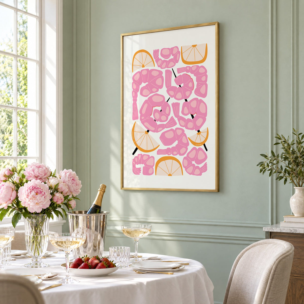 pink shrimp skewers orange wedges print in a brass frame on a sage wall above a brunch table with champagne and peonies, seen at an angle