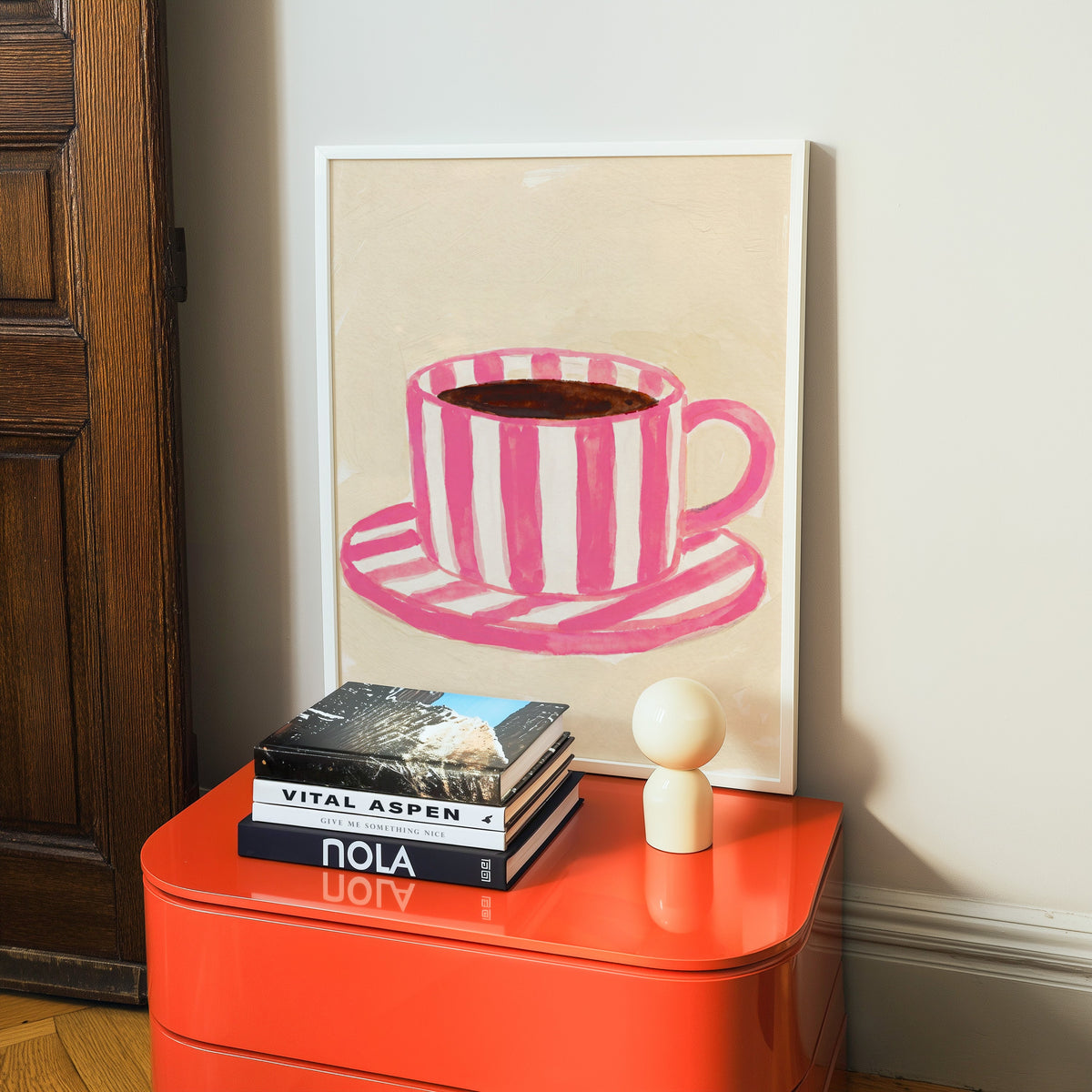 Watercolor coffee cup print in a white frame on a glossy orange cabinet with books