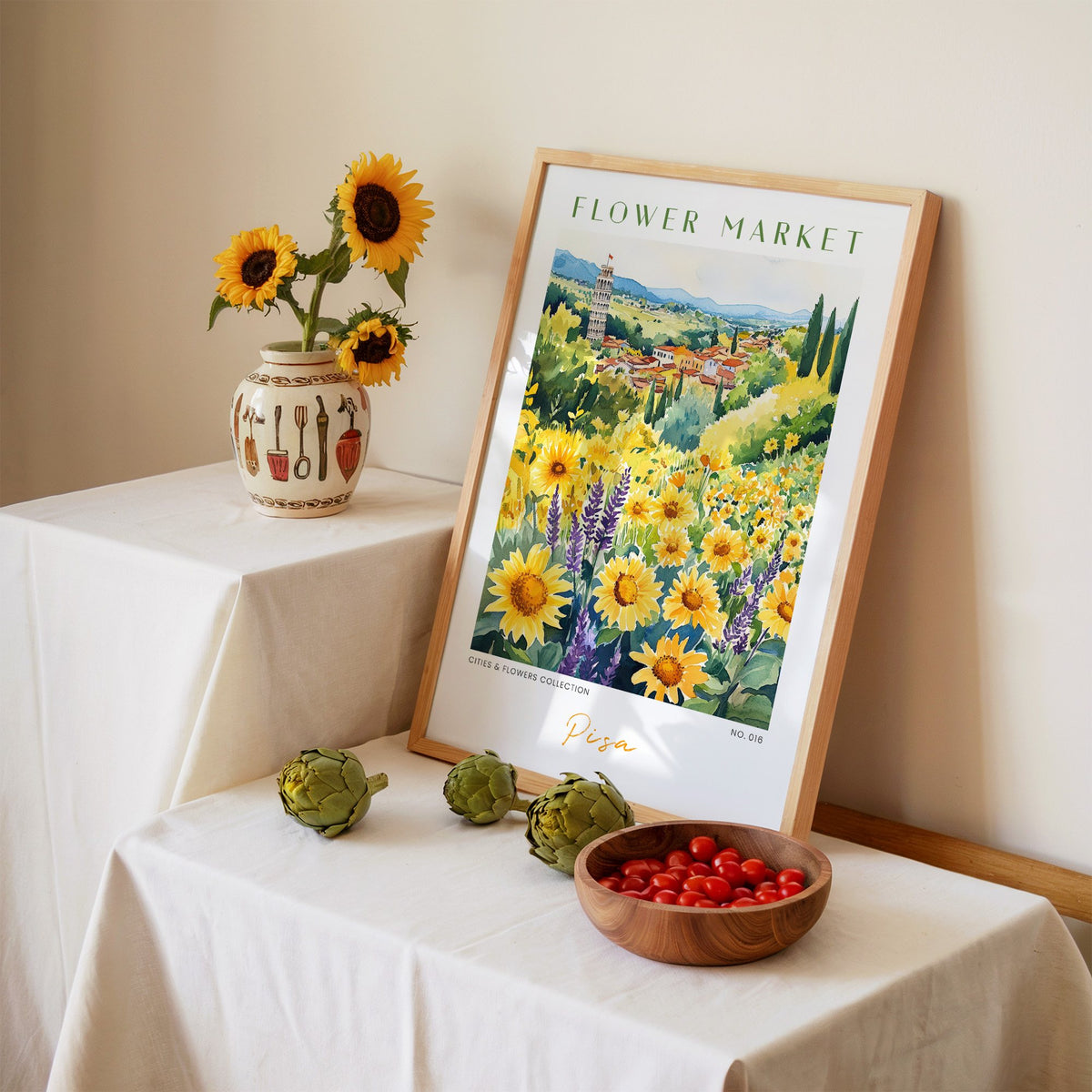 Pisa flower market print in an oak frame leaning on a linen-draped table beside a vase of sunflowers