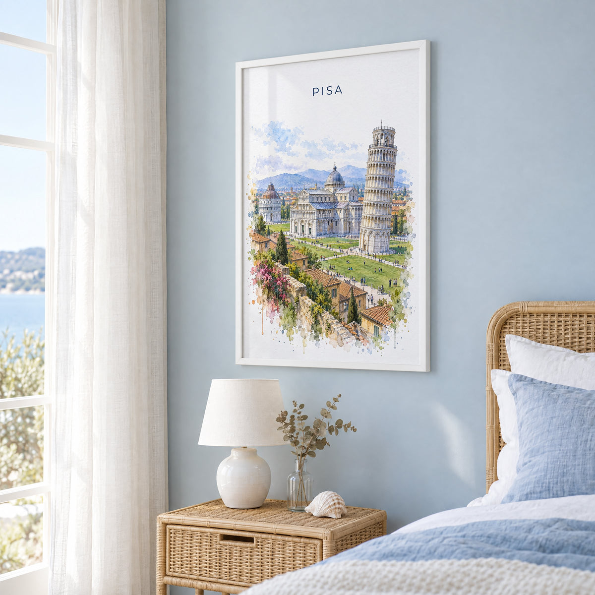 Pisa watercolor print in a white frame on a pale blue wall beside a rattan bed in a coastal bedroom