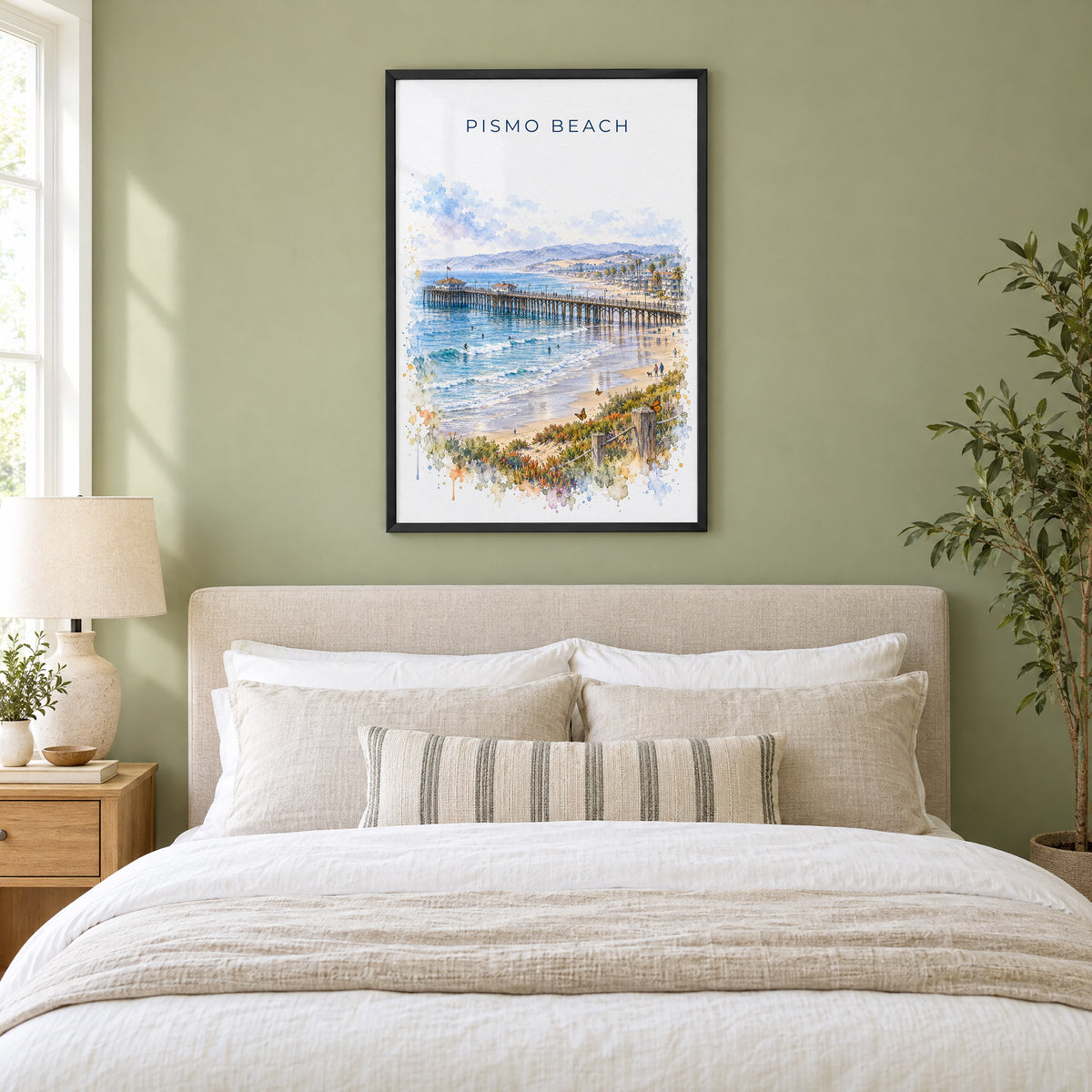 Pismo Beach watercolor print in a black frame above an upholstered headboard in a sage green bedroom