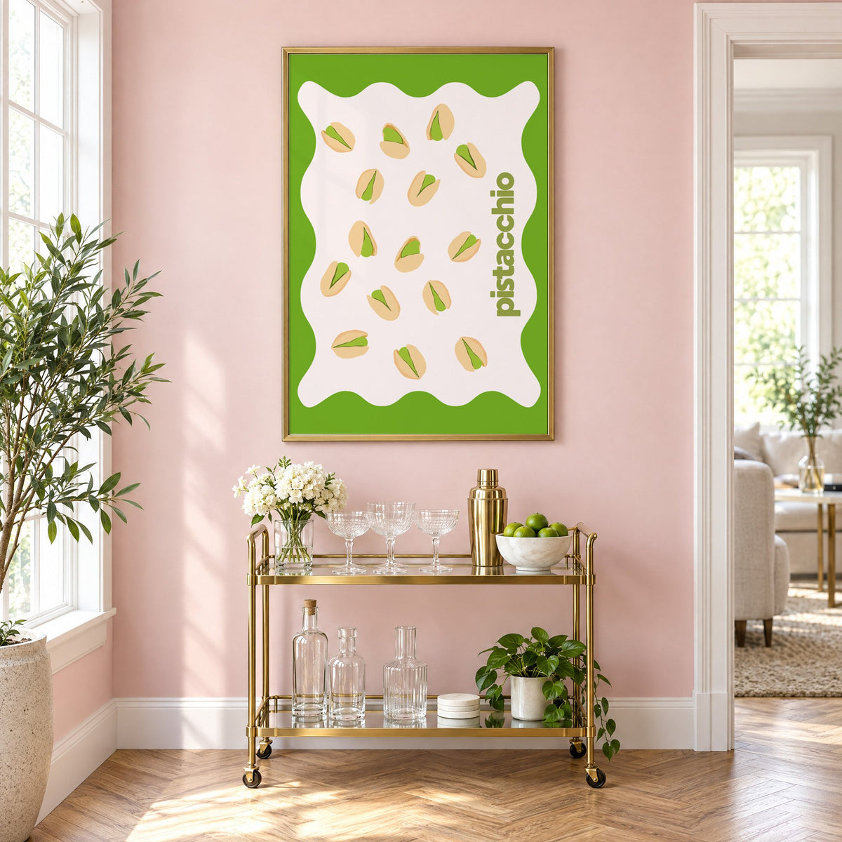 pistacchio vertical type pistachio nuts print in a brass frame on a blush pink wall above a gold bar cart with glassware