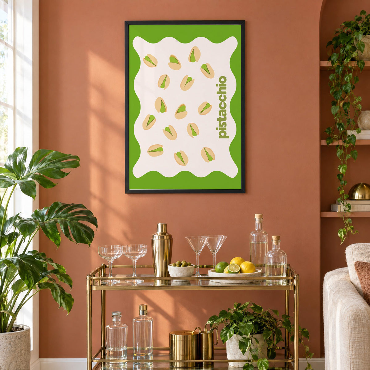pistacchio vertical type pistachio nuts print in a black frame on a terracotta wall above a brass bar cart with coupes and citrus